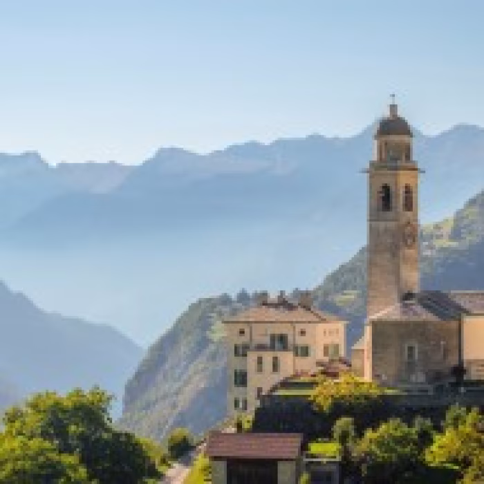 Historische Kirche in Graubünden mit Bergdorf und Alpen im Hintergrund